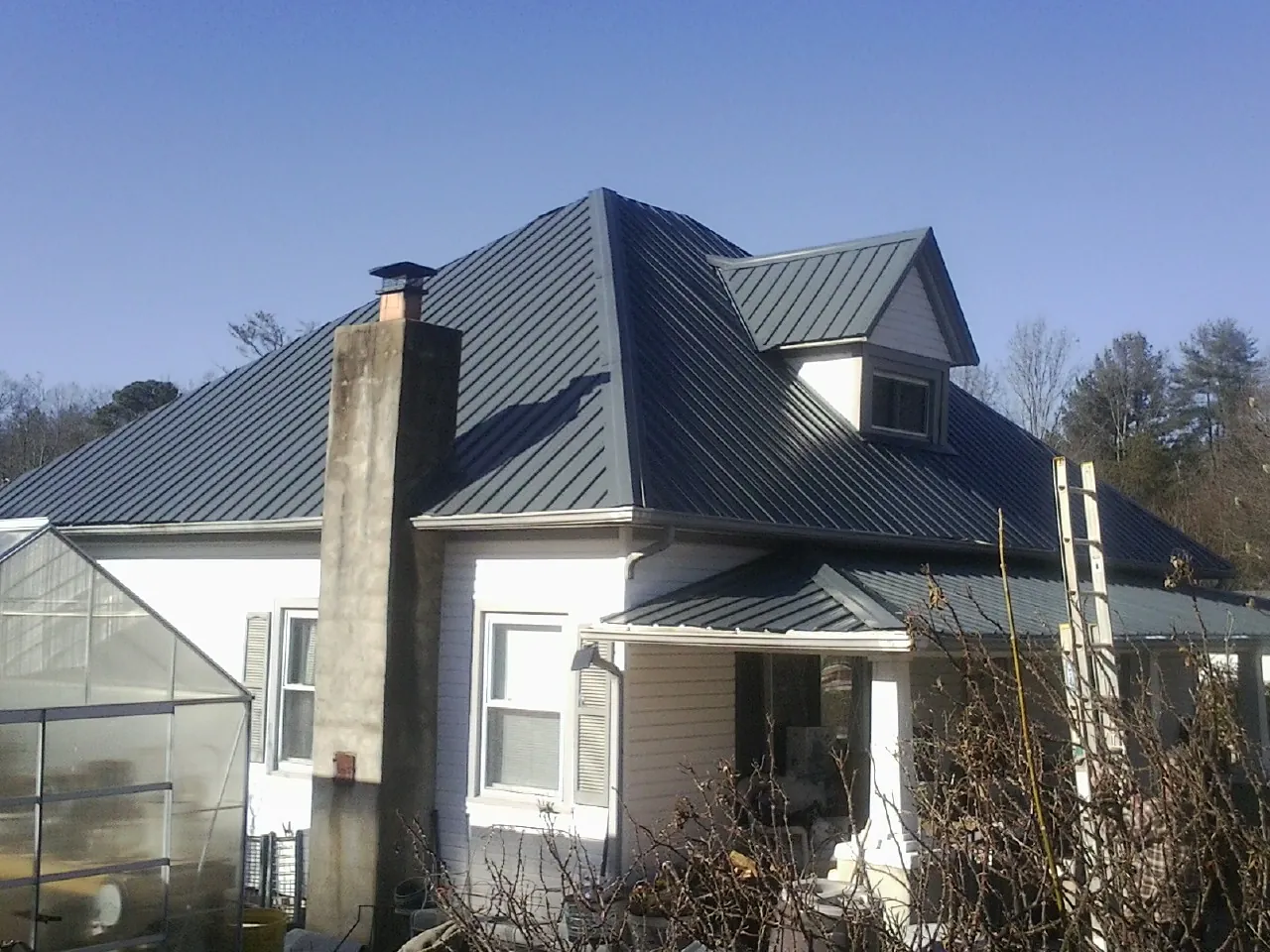 Dark blue standing seam metal roof on a white farmhouse with dormer — Slate & Tile Roof Repair by Roofing Brothers in Allred