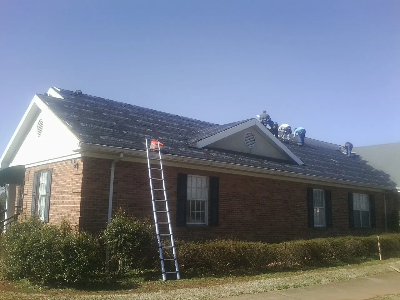 Crew tearing shingles off a brick ranch roof with a ladder set — Metal Roof Repair work by our crew in Allred