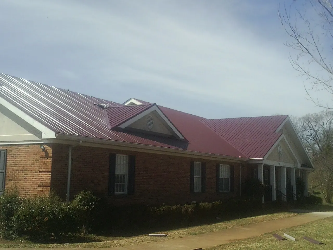 Red metal roof with gabled entries on a long brick building, from a Hail Damage Roof Repair job in Allred