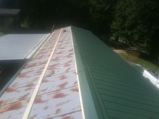 Old rusted panels beside newly installed green metal roofing — Wind Damage Roof Repair by Roofing Brothers in Allred