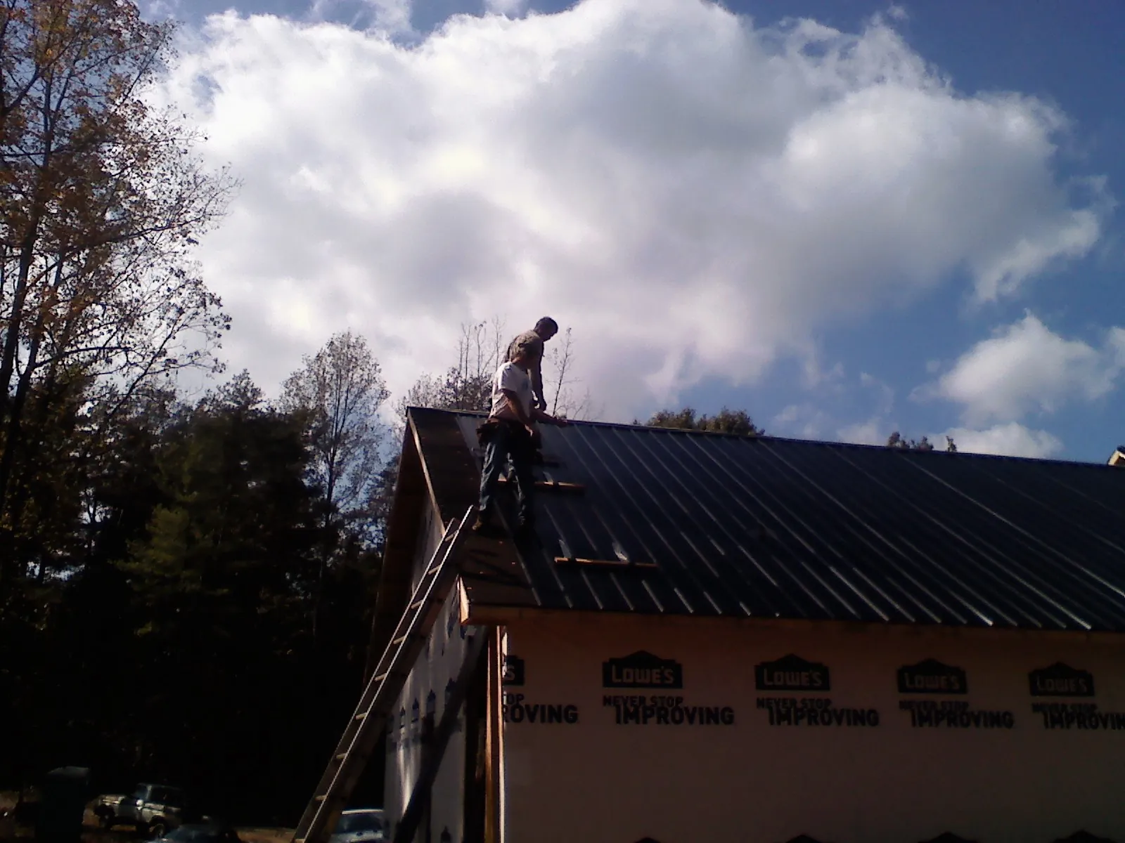 Roofer fastening dark metal panels high against a cloudy sky, from a Roof Inspection job in Allred