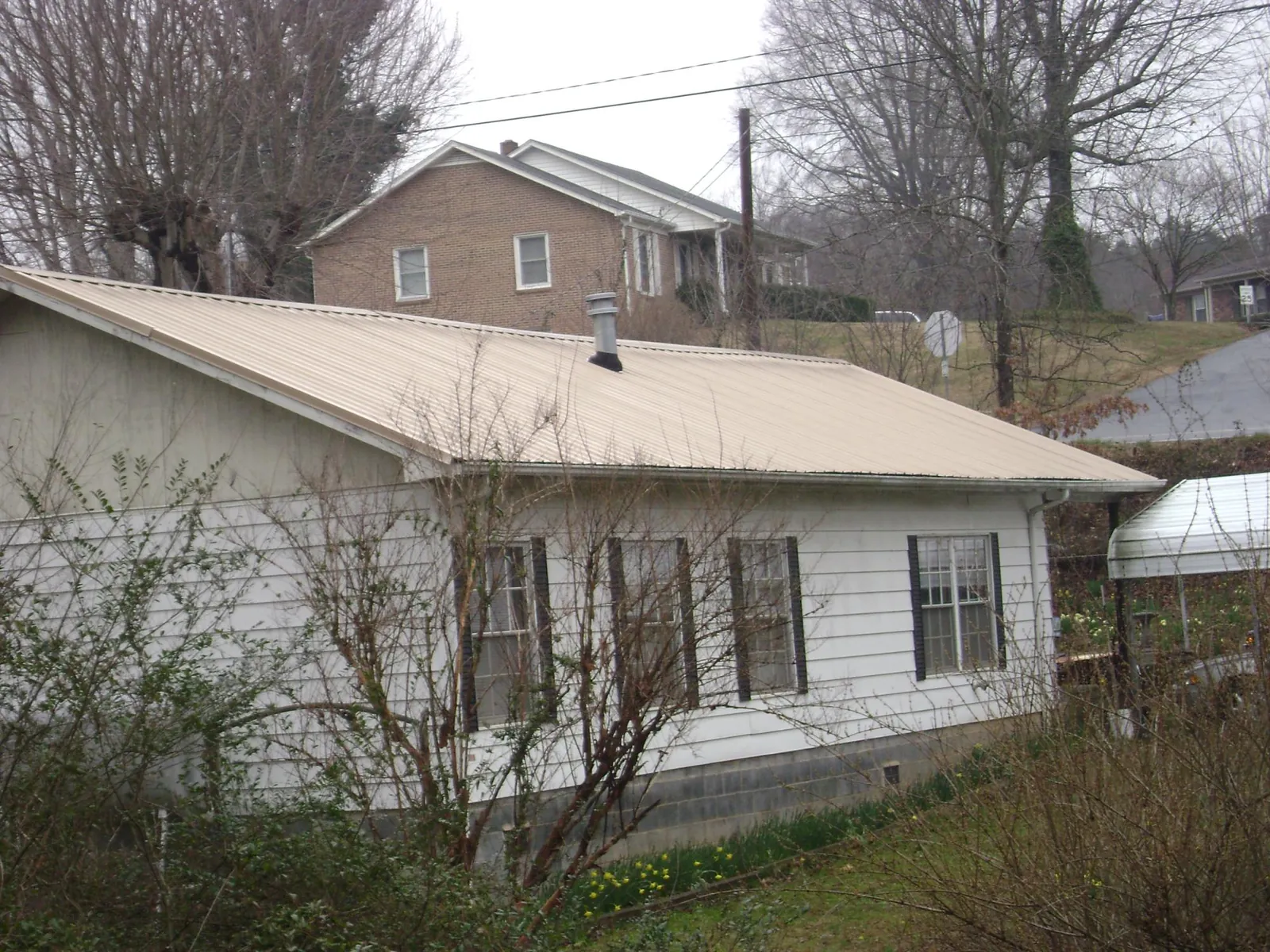 Tan metal roof on a white sided house set into a hillside — Commercial Roofing by Roofing Brothers in Allred